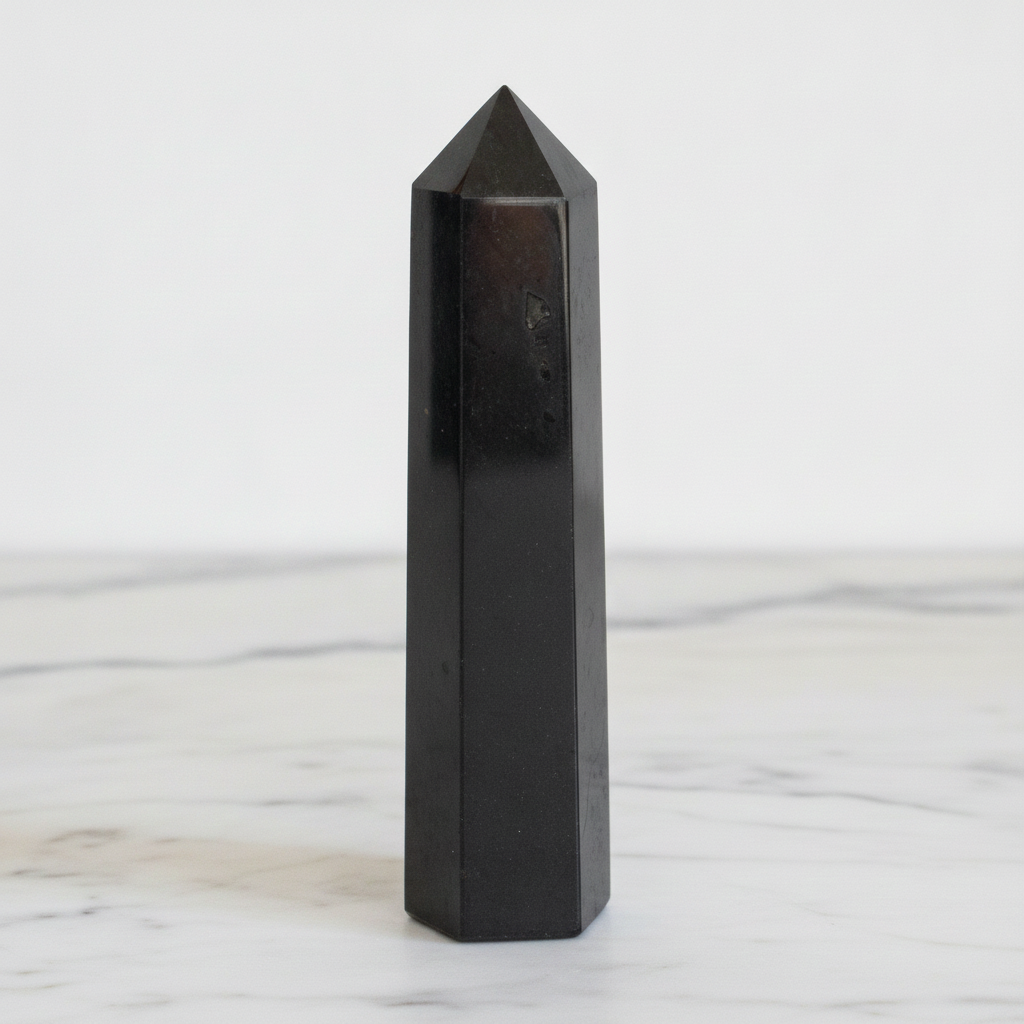 Black tourmaline obelisk point on a marble worktop in daylight