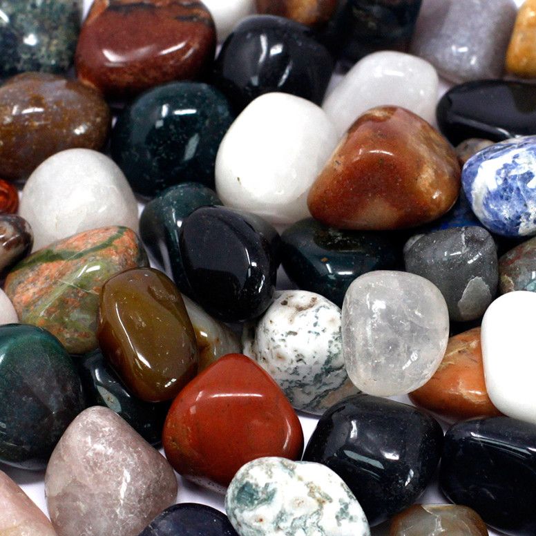 A pile of mixed tumbled gemstones in greens, reds and creams on cotton-rag paper - view 9