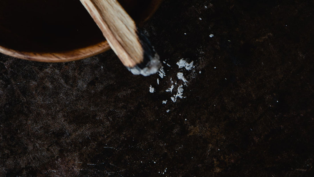 Salt being poured from a wooden bowl onto a dark surface