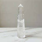 Clear quartz obelisk point on a marble worktop in daylight