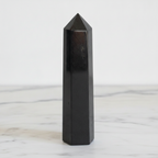 Black tourmaline obelisk point on a marble worktop in daylight