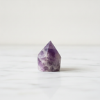 Polished amethyst crystal point on a pale marble surface against a white wall