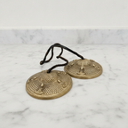 Tibetan tingsha bells joined by their cord, resting on a marble worktop