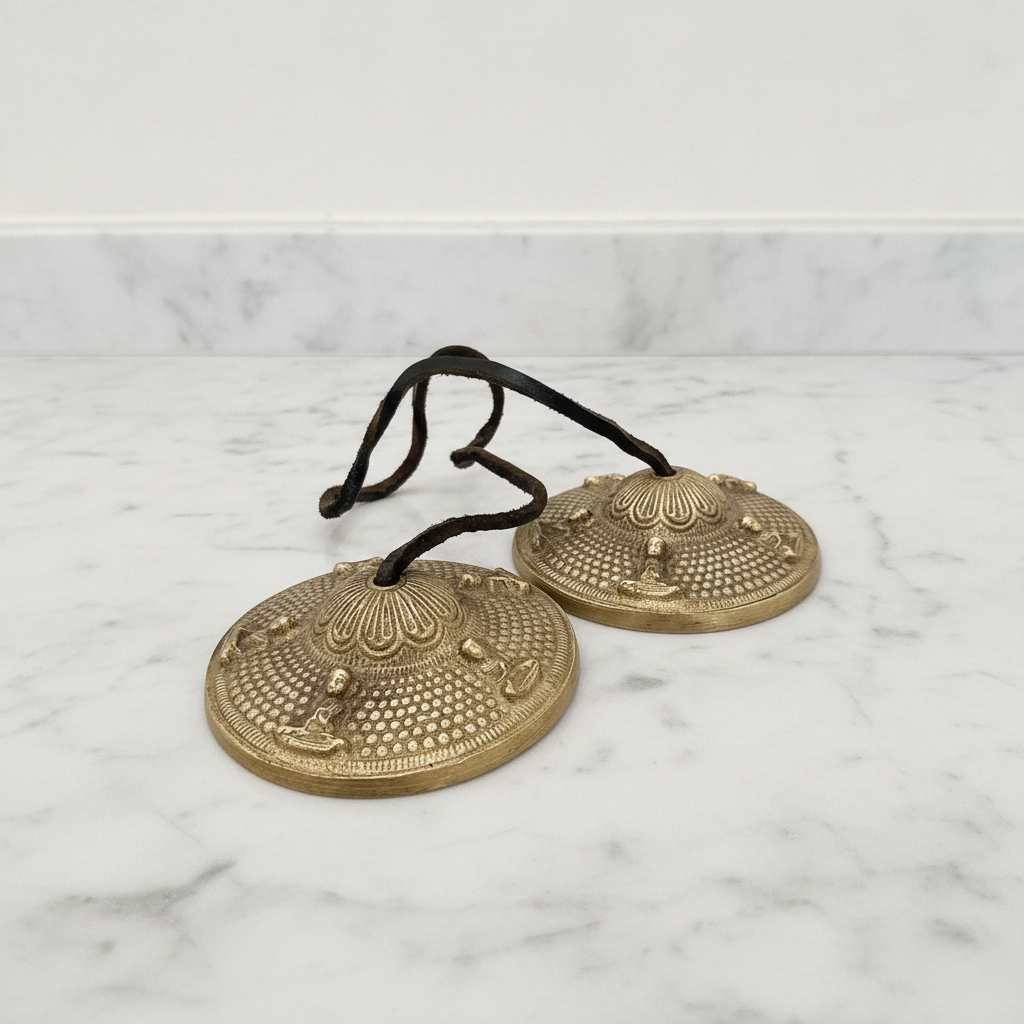 Tibetan tingsha bells joined by their cord, resting on a marble worktop