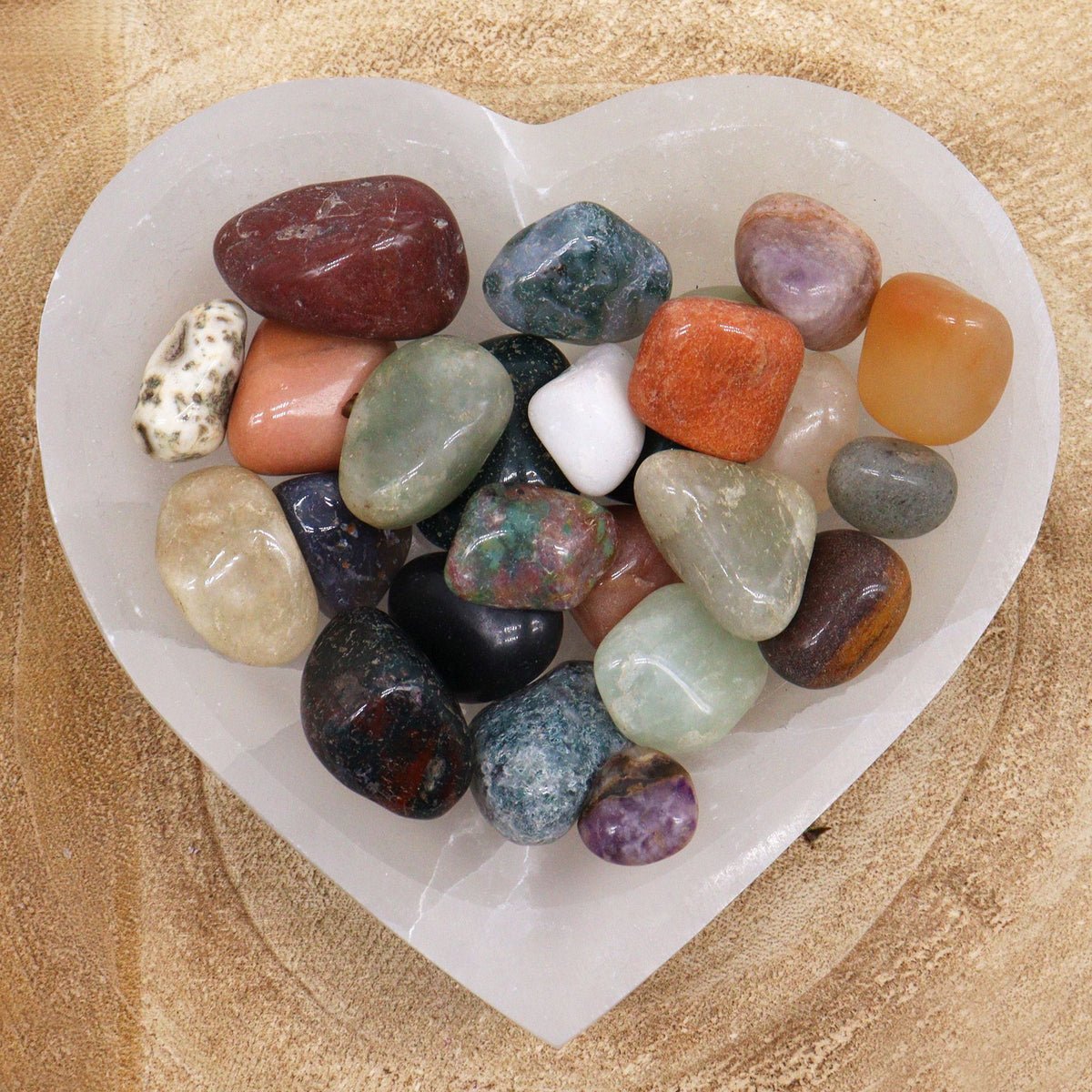 A pile of mixed tumbled gemstones in greens, reds and creams on cotton-rag paper - view 4