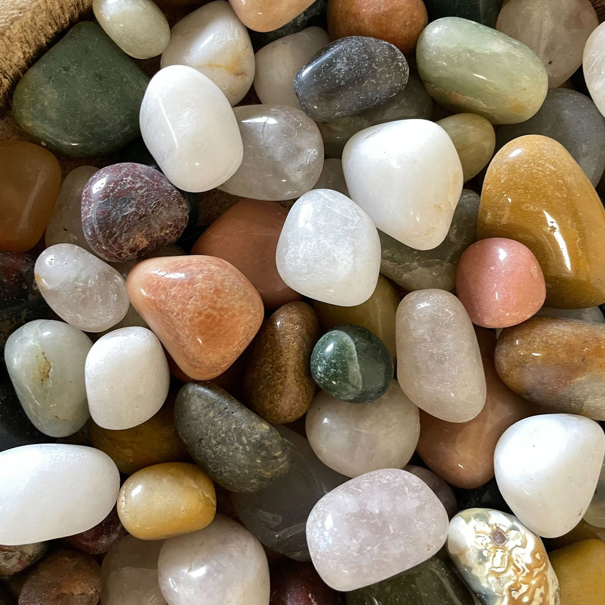 A pile of mixed tumbled gemstones in greens, reds and creams on cotton-rag paper - view 3