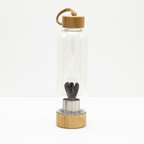 Amethyst crystal glass water bottle with a carved angel inside on a clean white surface against a white wall