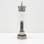 Amethyst crystal glass water bottle with an obelisk inside on a clean white surface against a white wall