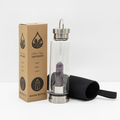 Amethyst crystal glass water bottle with an obelisk inside on a clean white surface against a white wall