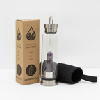 Amethyst crystal glass water bottle with an obelisk inside on a clean white surface against a white wall