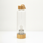 Clear quartz crystal glass water bottle with a carved angel inside on a clean white surface against a white wall