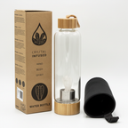 Clear quartz crystal glass water bottle with a carved angel inside on a clean white surface against a white wall