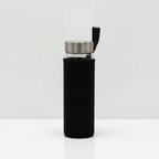 Red jasper crystal glass water bottle with crystal chips inside on a clean white surface against a white wall