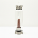 Red jasper crystal glass water bottle with an obelisk inside on a clean white surface against a white wall