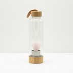 Rose quartz crystal glass water bottle with a carved angel inside on a clean white surface against a white wall