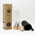 Rose quartz crystal glass water bottle with a carved angel inside on a clean white surface against a white wall
