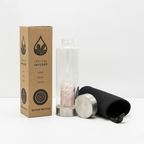 Rose quartz crystal glass water bottle with crystal chips inside on a clean white surface against a white wall