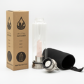 Rose quartz crystal glass water bottle with an obelisk inside on a clean white surface against a white wall