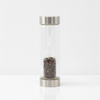 Tiger's eye crystal glass water bottle with crystal chips inside on a clean white surface against a white wall