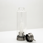 Clear quartz crystal glass water bottle on a clean white surface against a white wall