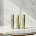 Epidote six face obelisk on a marble table with a marble wall behind