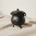 Cast iron cauldron with triple moon symbol and lid on natural linen