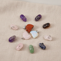 Twelve assorted gemstone mini skull pendants on natural linen