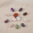 Twelve assorted gemstone mini skull pendants on natural linen