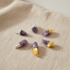 Six assorted amethyst gold and silver plated pendants on natural linen