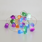 Mixed gemstone crystal fairy lights on a clean white surface against a white wall