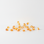 Orange jade crystal fairy lights on a clean white surface against a white wall