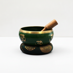 Green singing bowl on its cushion with the wooden striker resting in the bowl