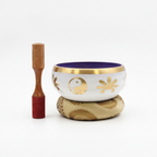 White and purple singing bowl with gold yin yang symbols, on its cushion beside the striker