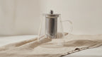 Glass infuser teapot with stainless steel filter on natural linen