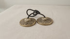 A pair of brass tingsha cymbals joined by a black cord, on cotton canvas video
