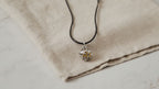 Silver angel bell pendant on a black cord resting on natural linen