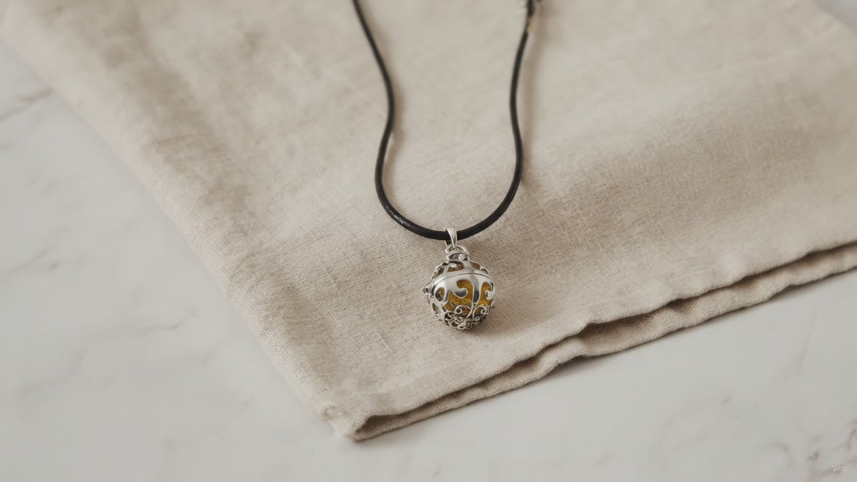 Silver angel bell pendant on a black cord resting on natural linen