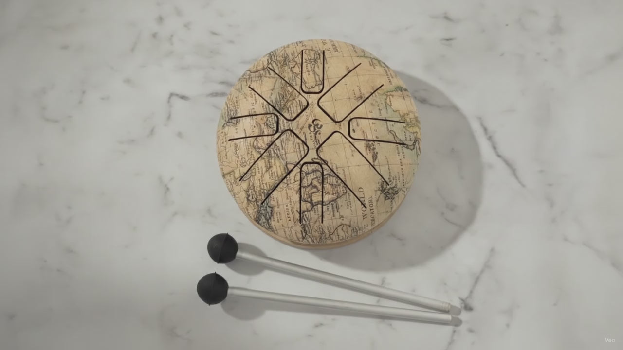 Small steel tongue drum in the Atlas world map design with two beaters, slow close-up