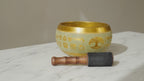 Large aluminium singing bowl with Buddha and Tree of Life engraving and wooden striker on marble, slow push-in