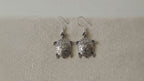 A pair of sterling silver turtle drop earrings on cotton canvas video