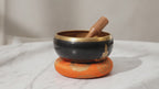 Large black and orange Buddha singing bowl set with cushion and striker on marble, slow push-in