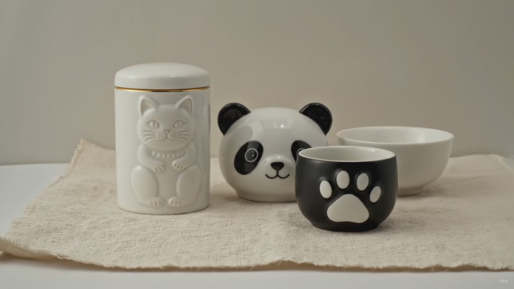 Panda-faced ceramic teapot with two cups and a golden hat lid, on cotton canvas video