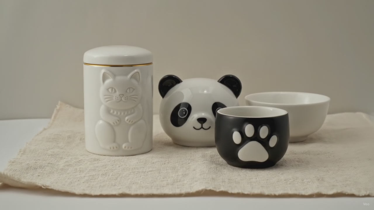 Panda-faced ceramic teapot with two cups and a golden hat lid, on cotton canvas video