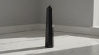 Black tourmaline six face obelisk point standing on marble in soft daylight, slow camera push-in