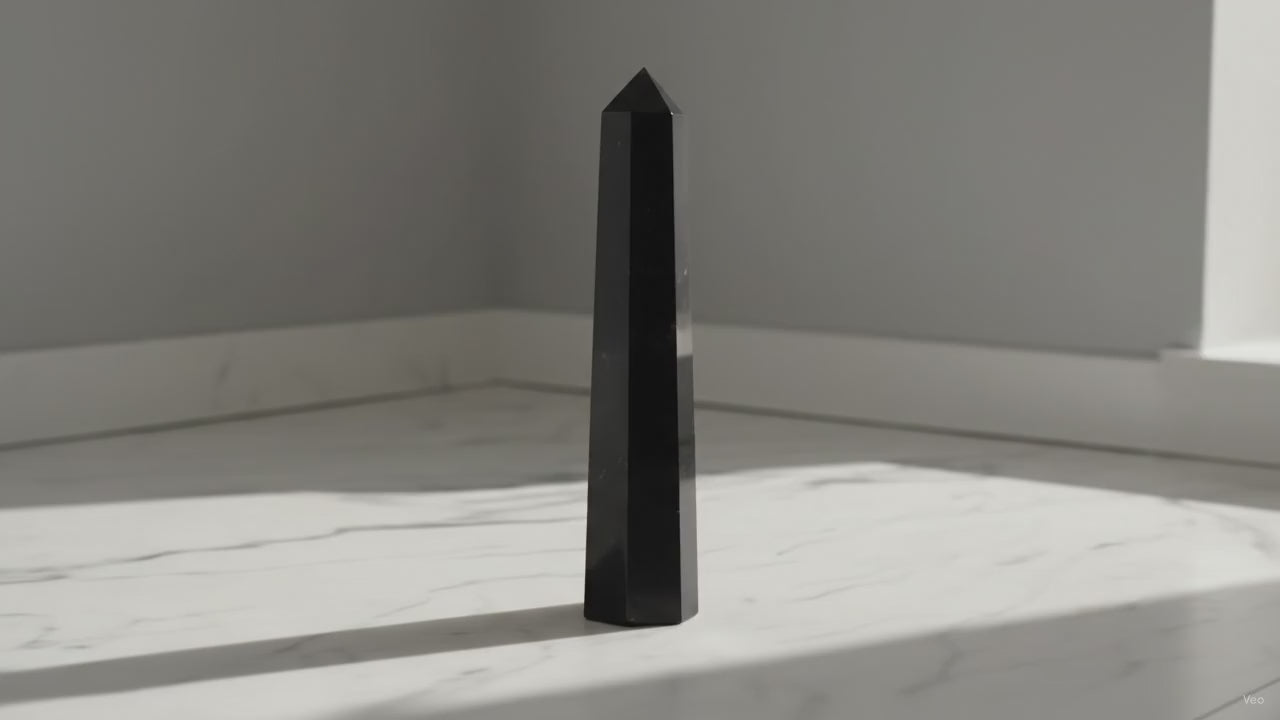 Black tourmaline six face obelisk point standing on marble in soft daylight, slow camera push-in