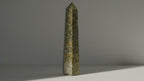 Epidote obelisk point standing alone as sunlight drifts across the wall behind it