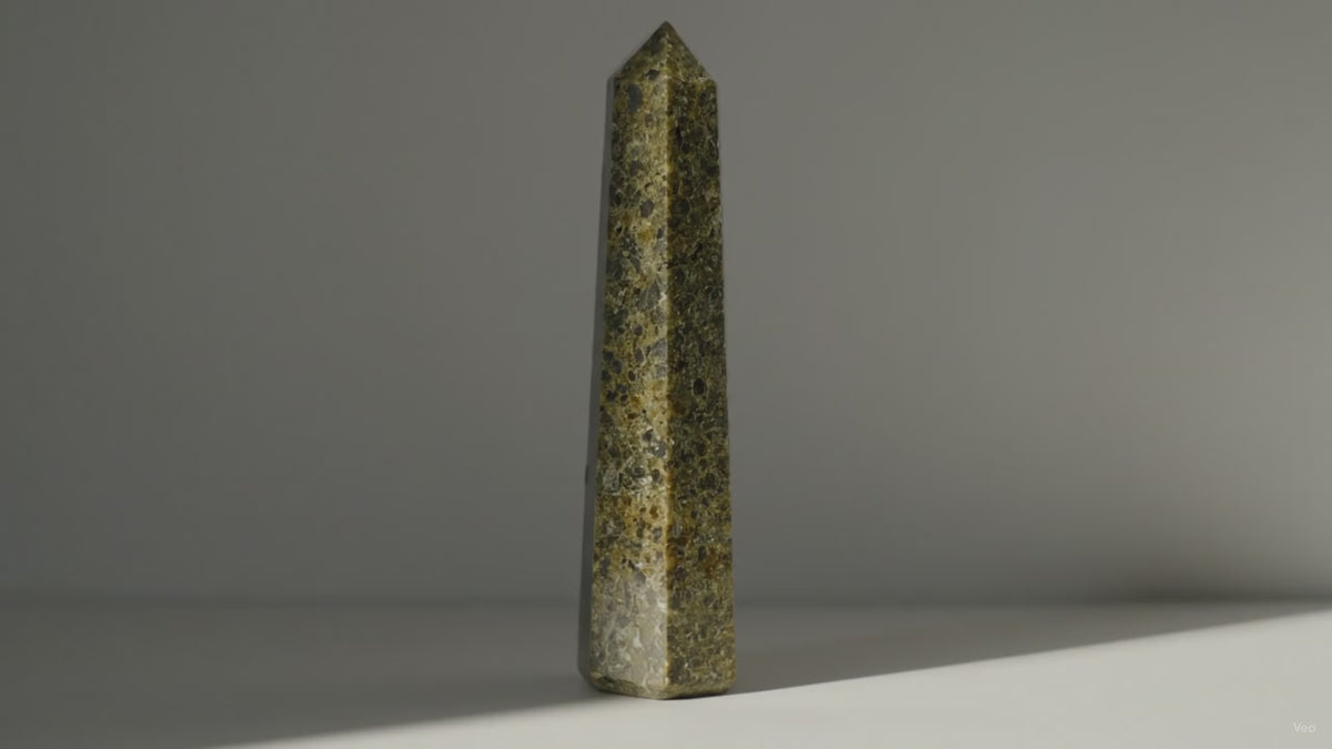 Epidote obelisk point standing alone as sunlight drifts across the wall behind it