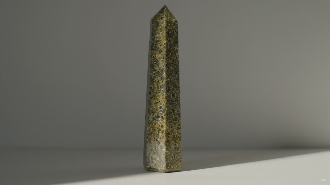 Epidote obelisk point standing alone as sunlight drifts across the wall behind it