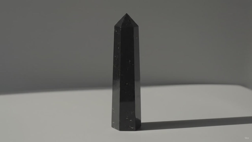 Black tourmaline obelisk point standing alone as soft light drifts across the wall
