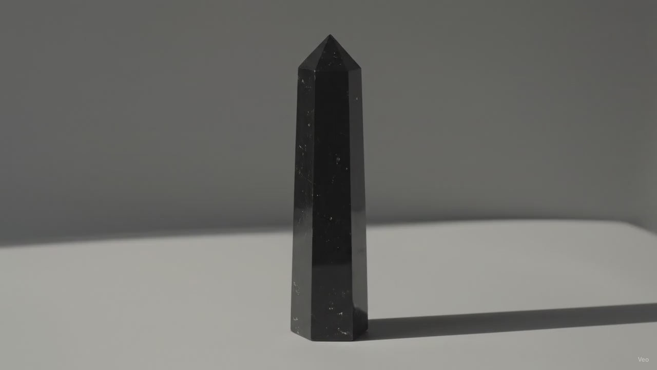 Black tourmaline obelisk point standing alone as soft light drifts across the wall